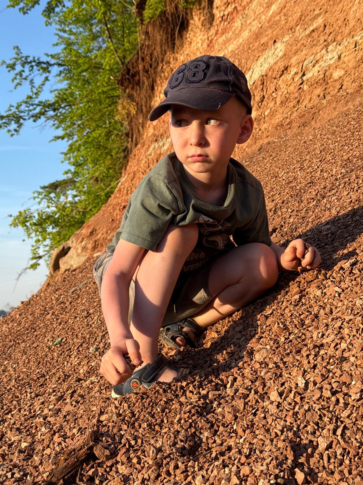 Child sits on gravel holding object in Chaikovsky