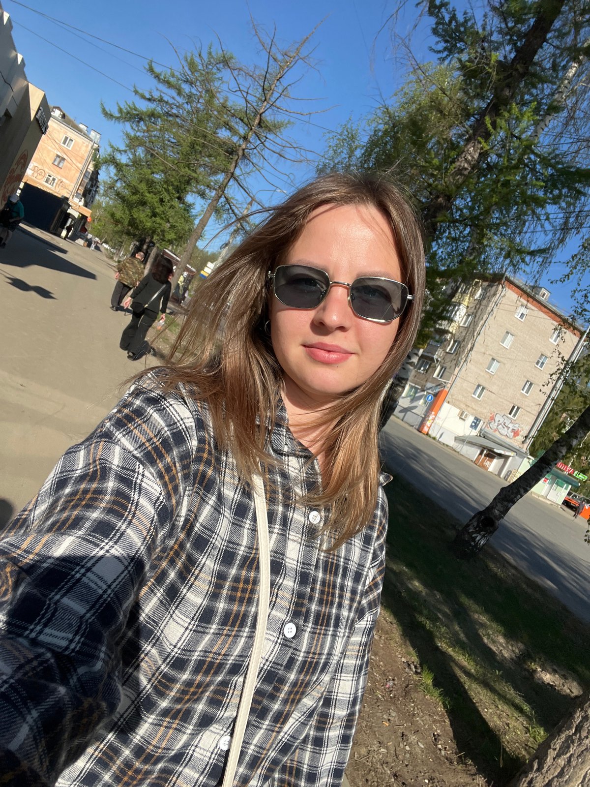 Woman takes selfie on tree-lined street in Izhevsk