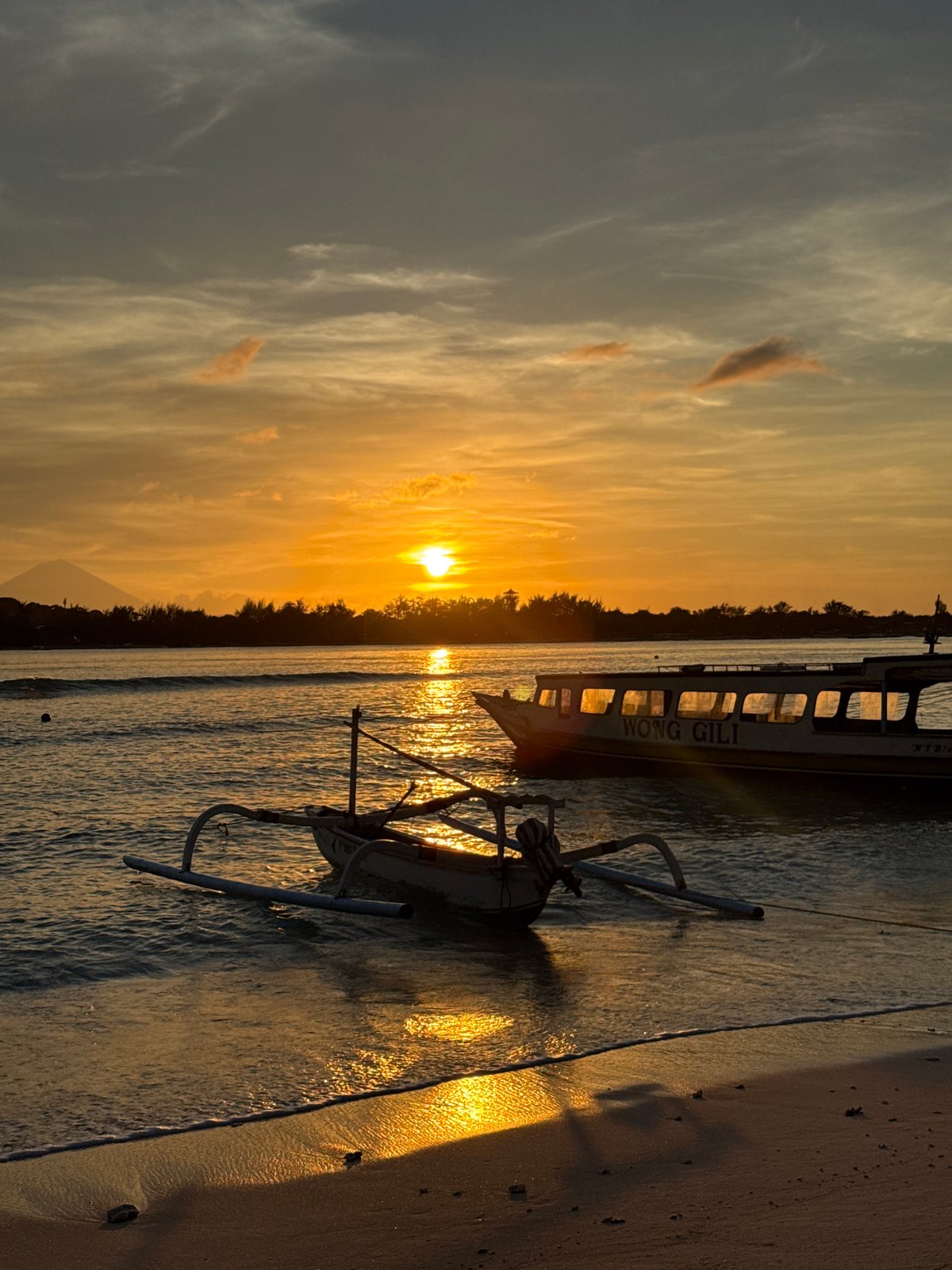 Indonesian beach sunset captured with traditional boats and tourist selfies