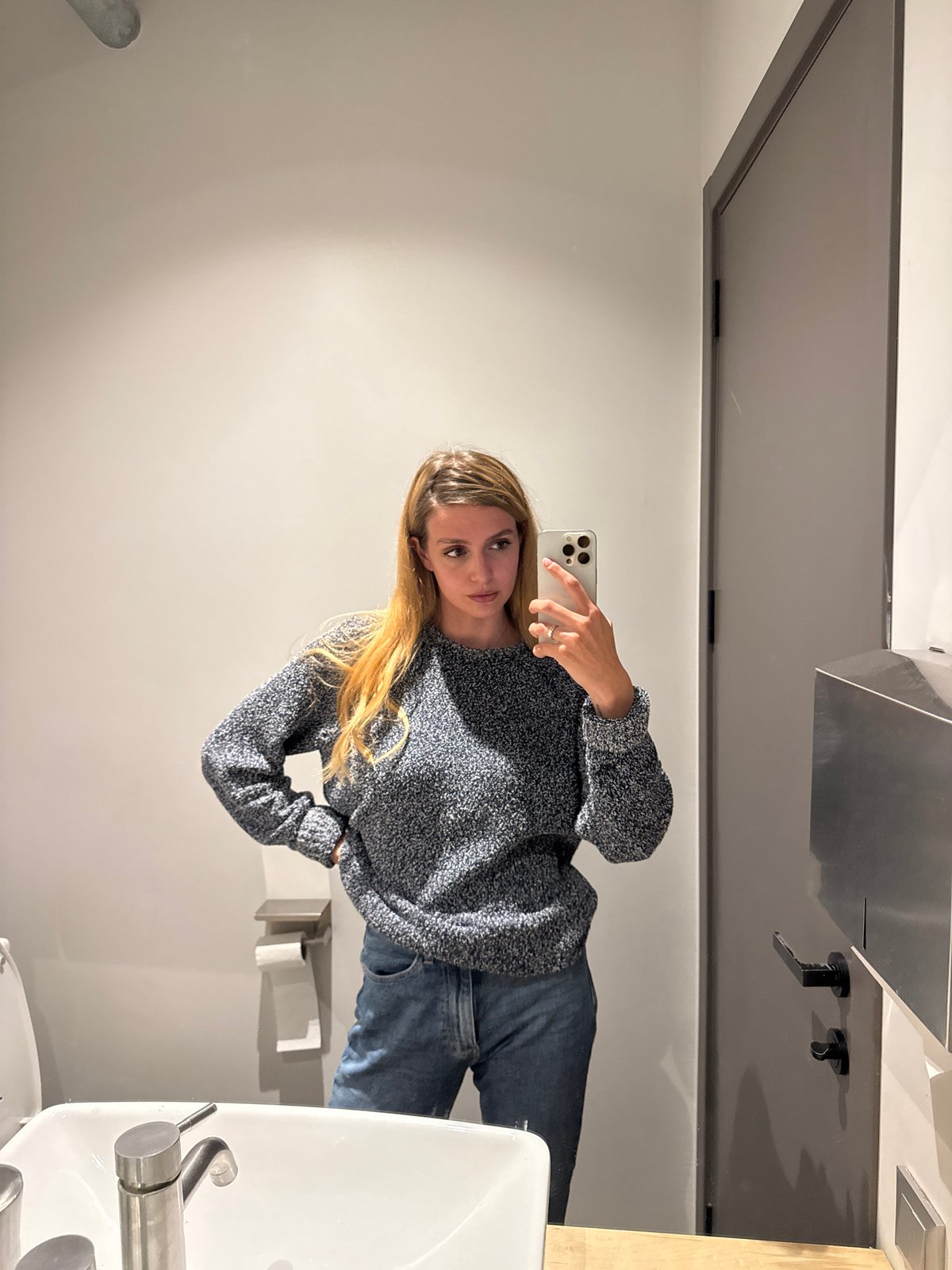 Woman takes bathroom mirror selfies in blue sweater