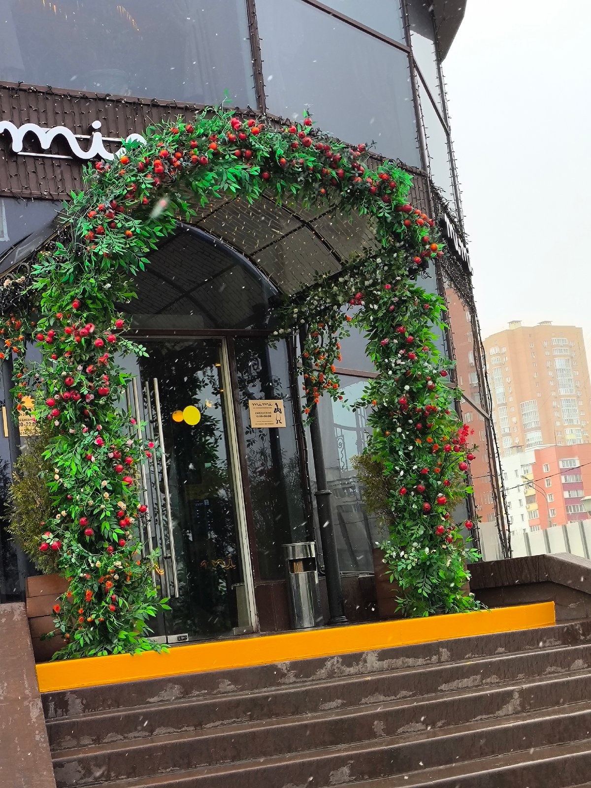 Commercial building entrance with decorative greenery archway documented