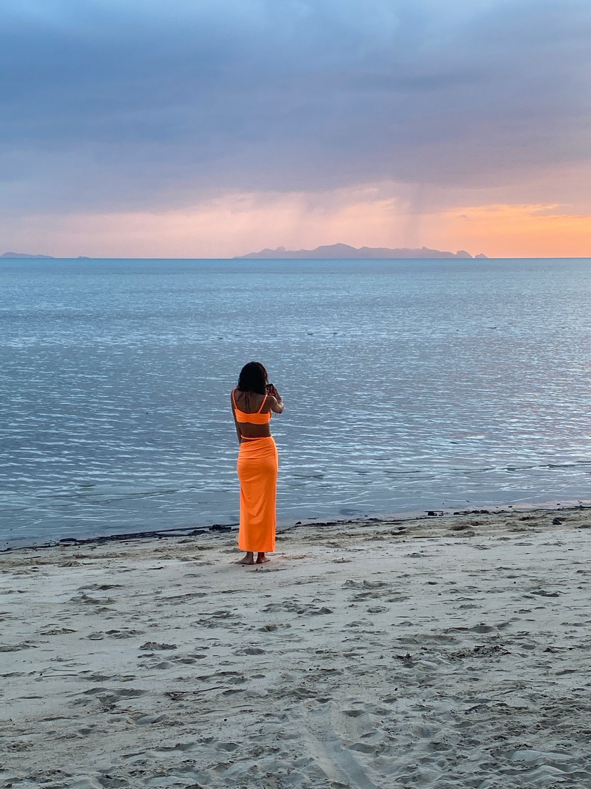 Orange outfit, Ko Samui beach, phone out at the water's edge