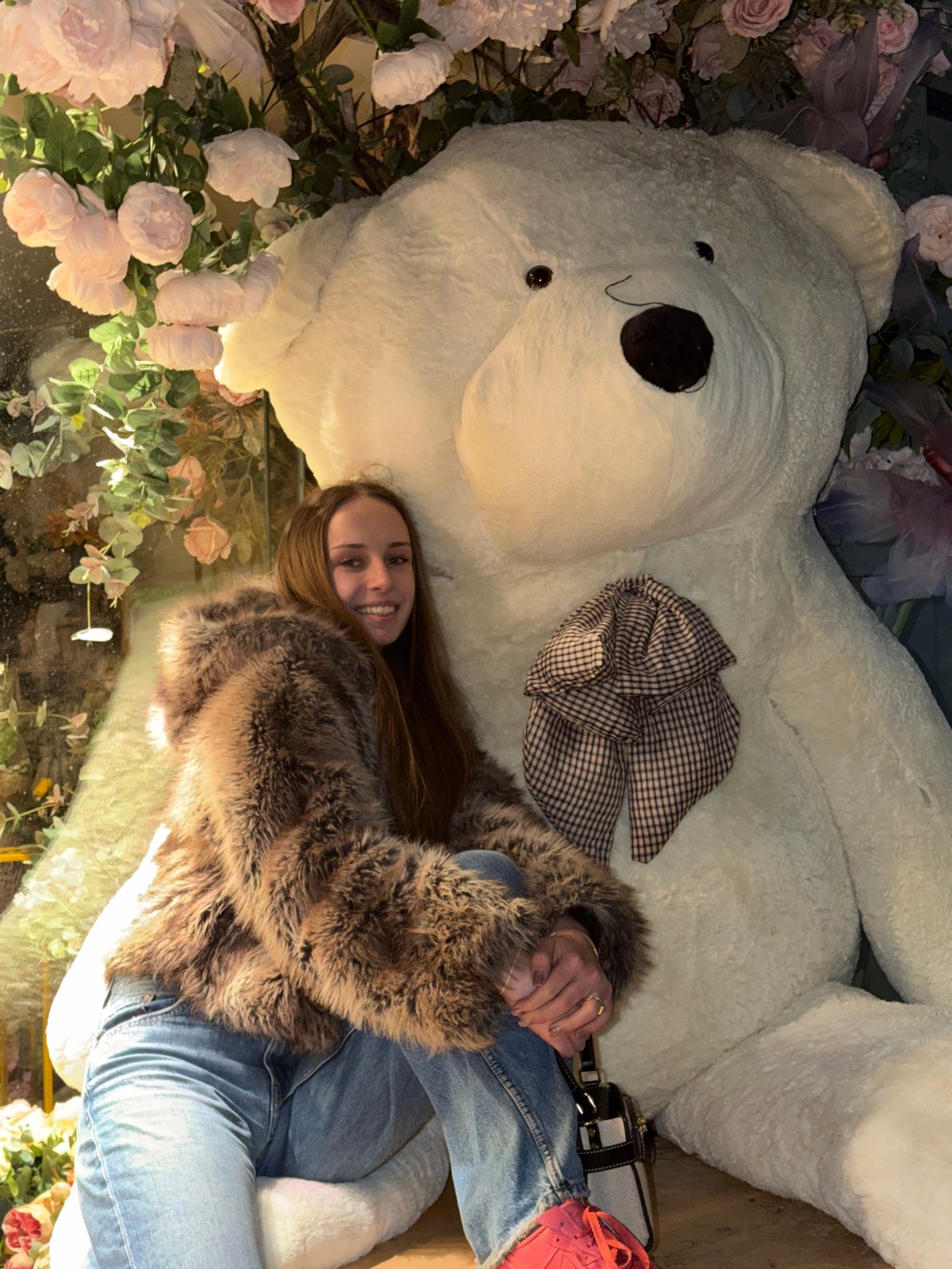 Woman poses with giant teddy bear in floral display