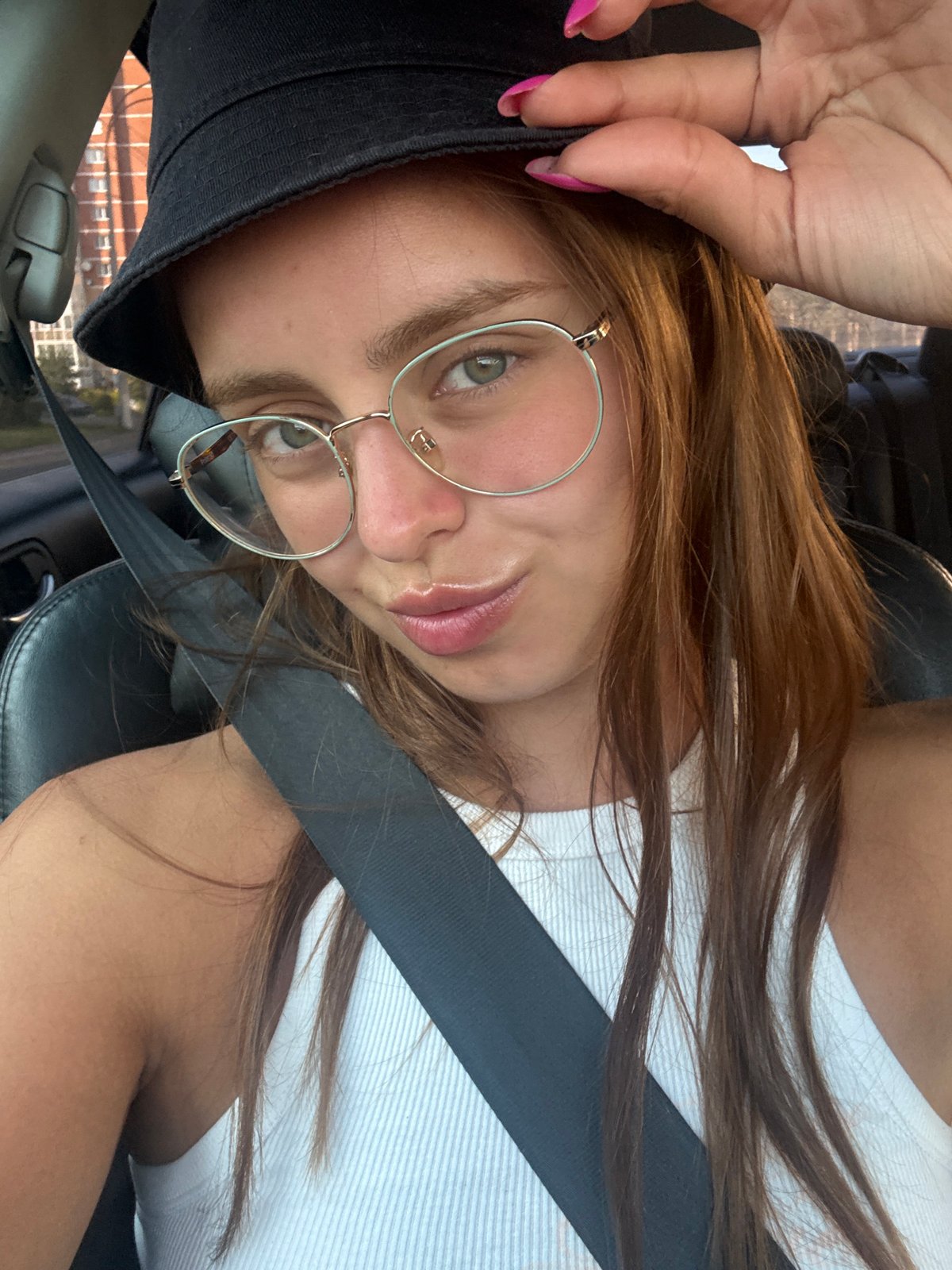 Parked outside an apartment building, adjusting a bucket hat