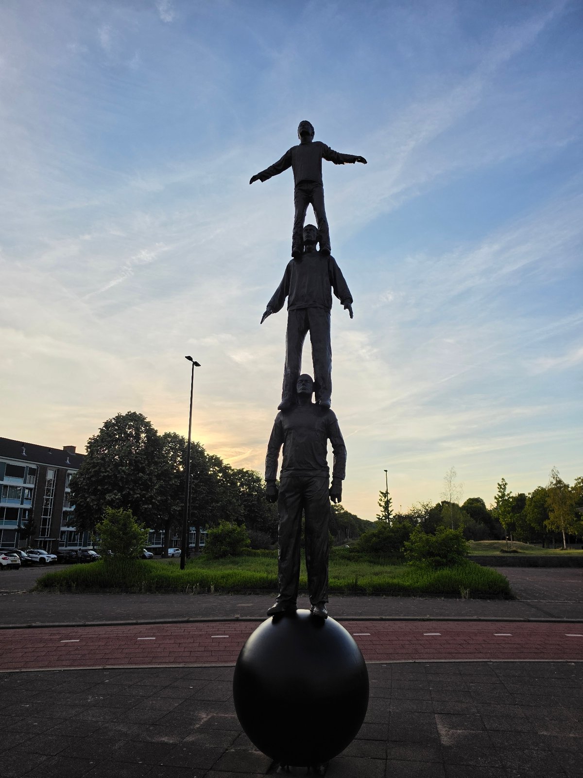 Stacked bronze figures rise in Rijswijk at dusk