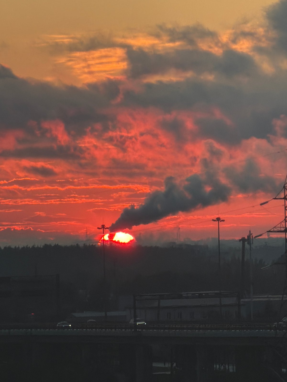 Industrial skyline at sunset, smoke rising against a fiery sky