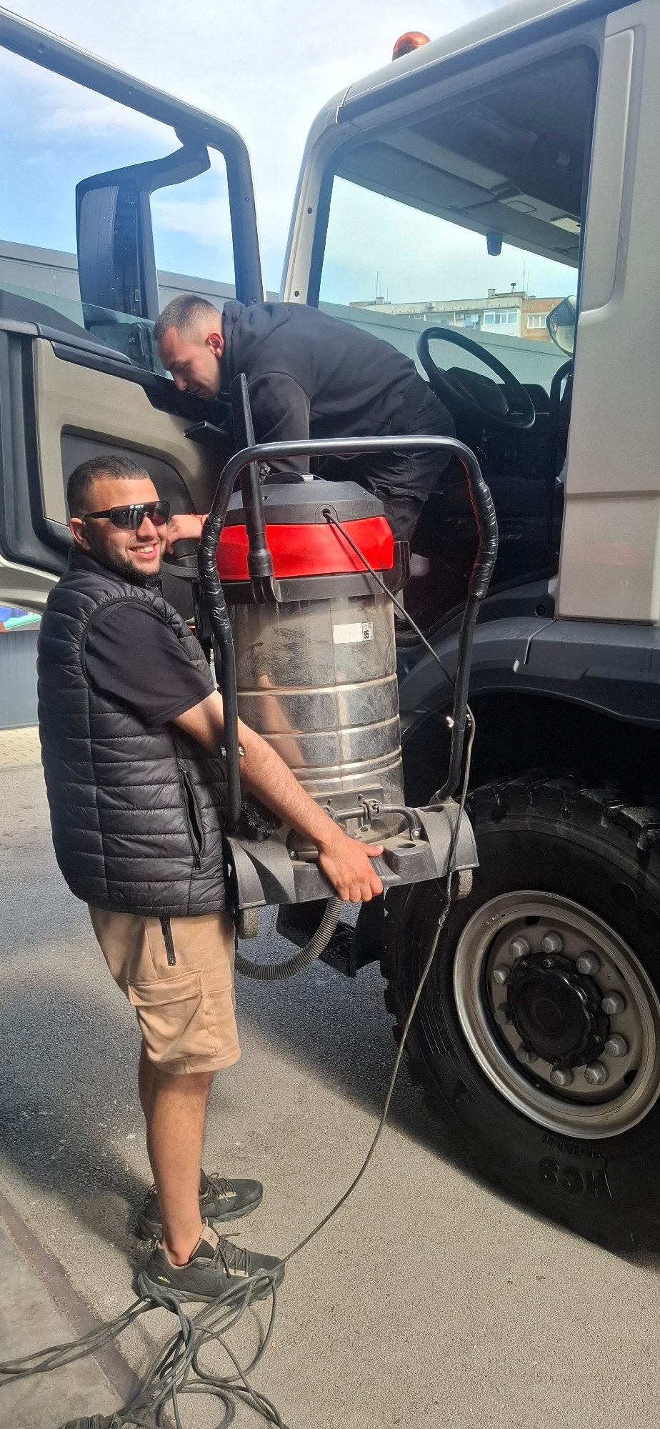 Two workers perform vehicle maintenance outdoors in daylight