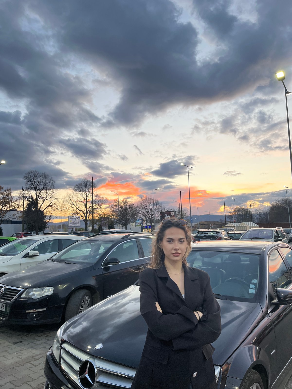 Woman poses with Mercedes at sunset in Bulgarian parking lot