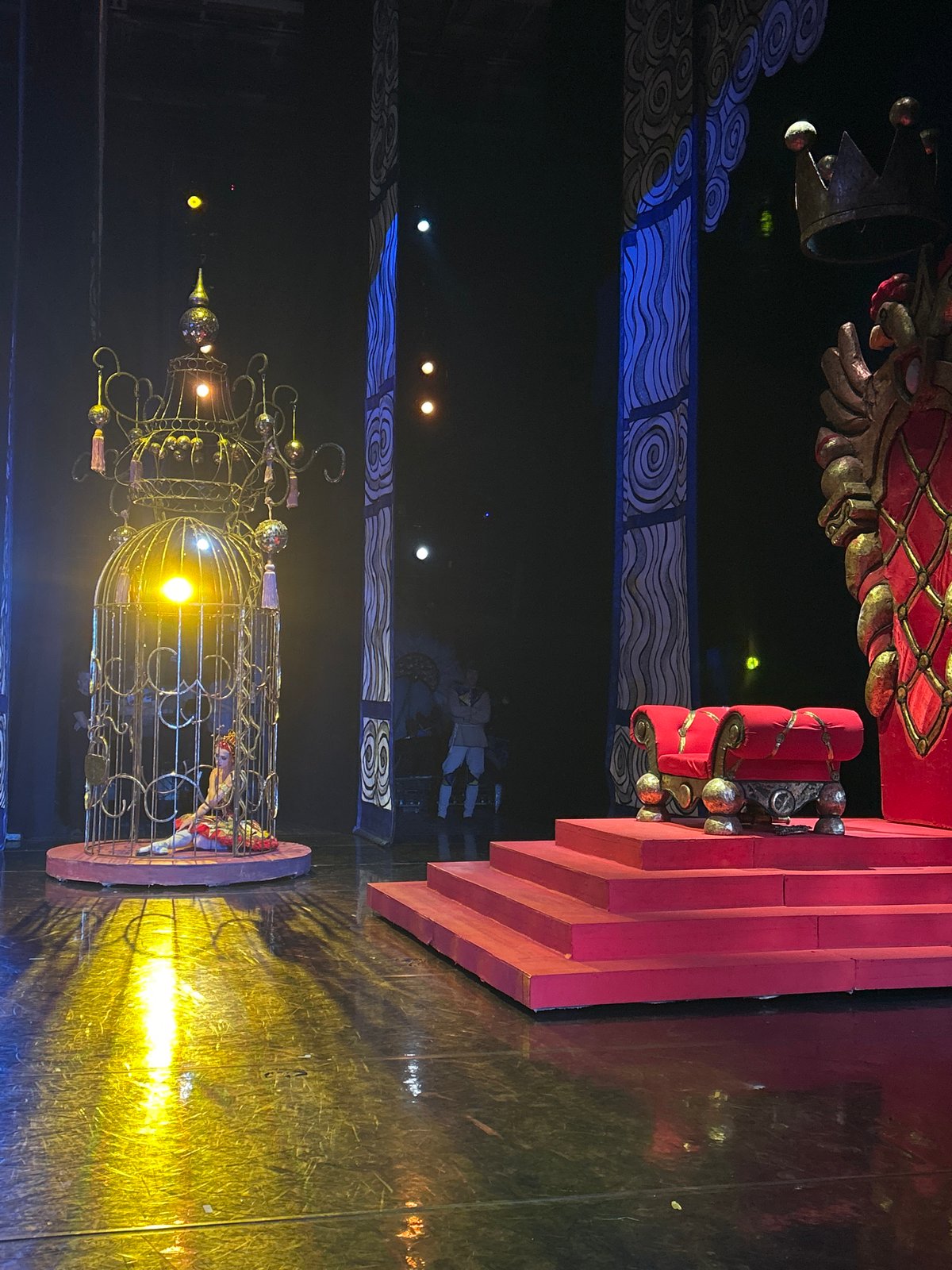 Theatrical stage set with gilded birdcage and dramatic lighting