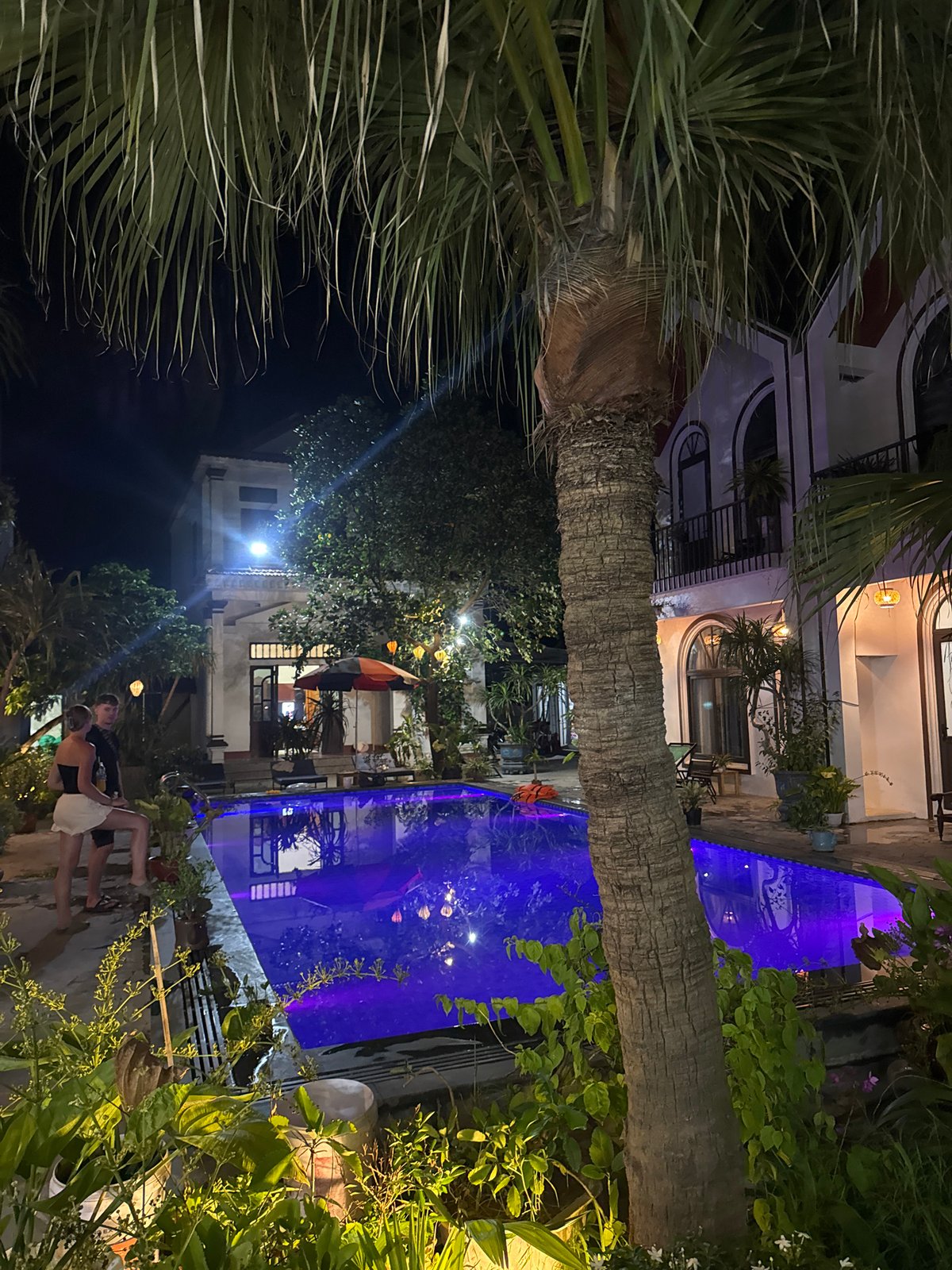 Evening resort gathering with illuminated pool and waterfront boats