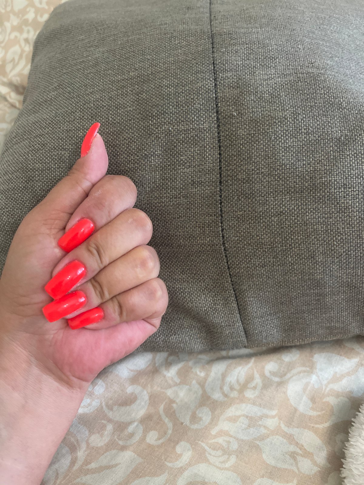 Person displays neon orange square nails on gray fabric