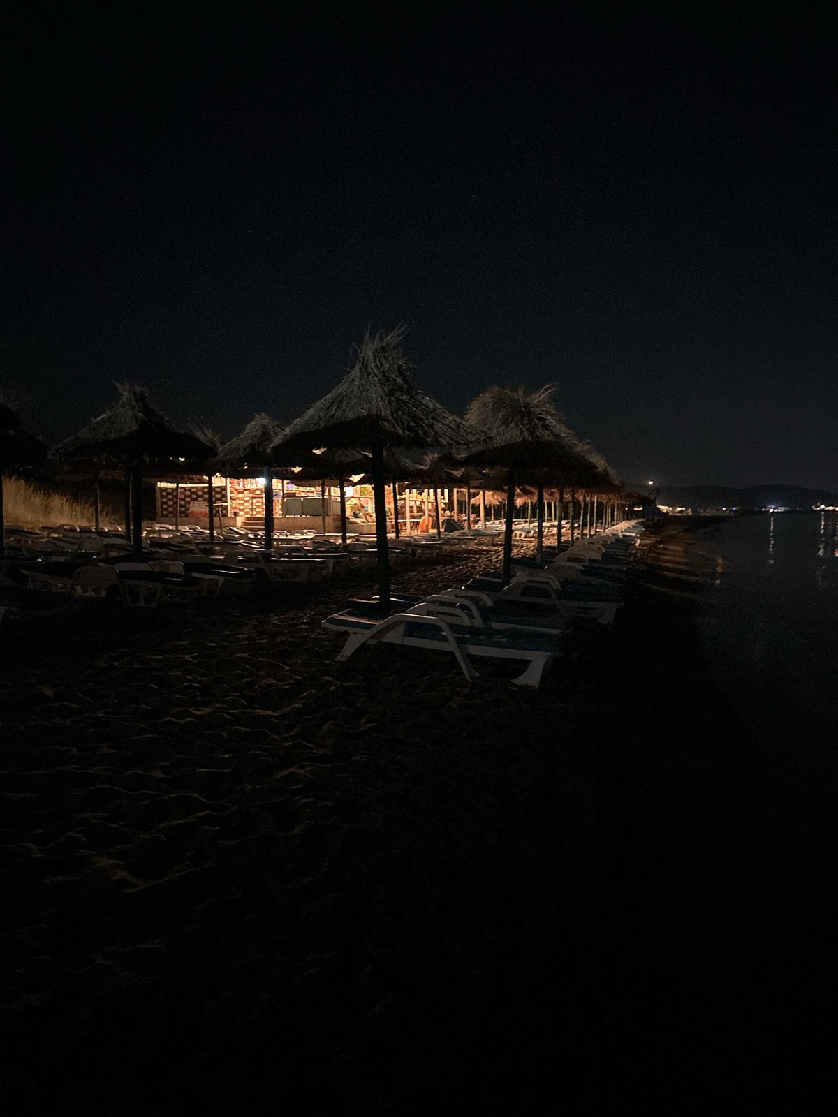 Empty beach and lit patio at a coastal venue after dark