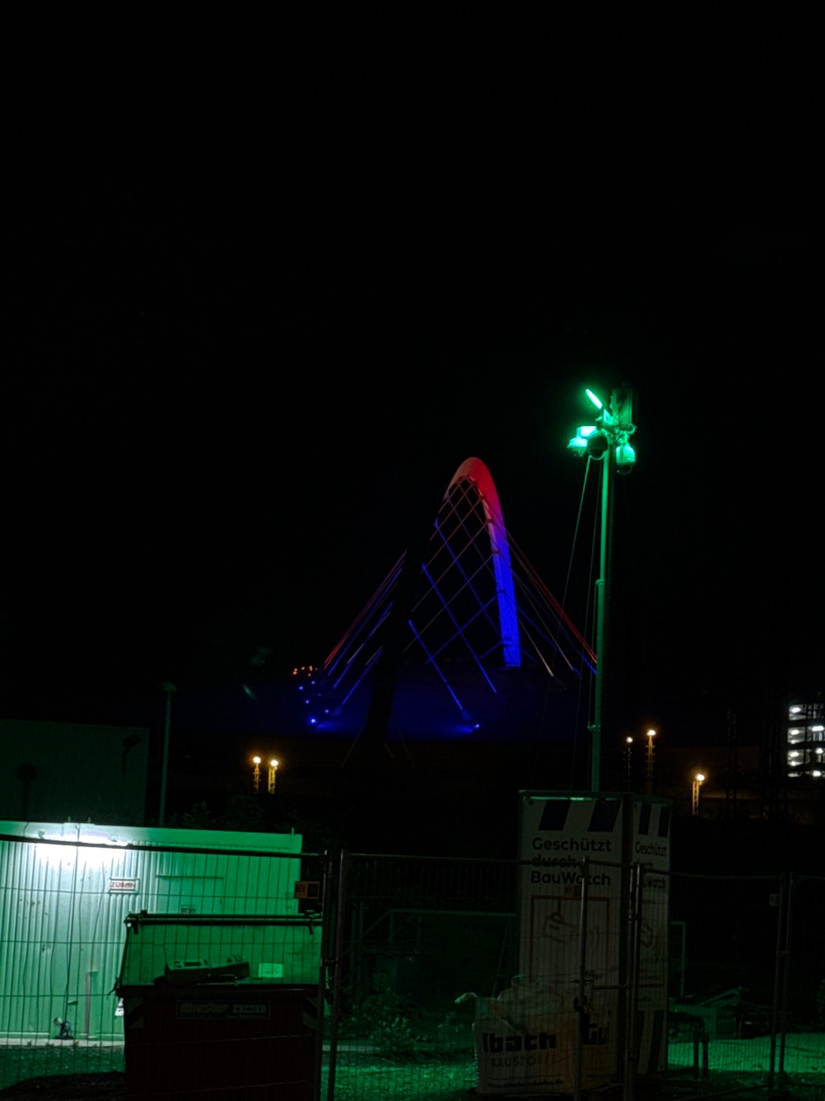 Cologne bridge lit in red-blue with construction equipment visible