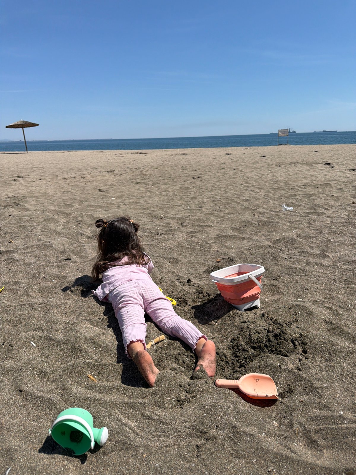 Child in pajamas plays with toys on dark sand beach