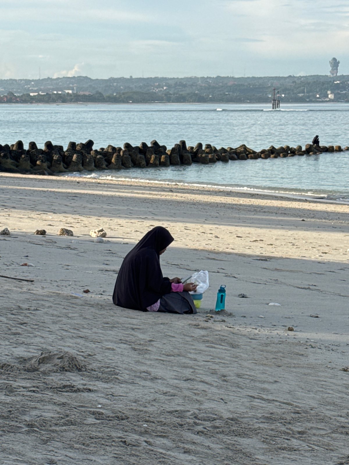 Woman sits on protected Kuta beach holding white object