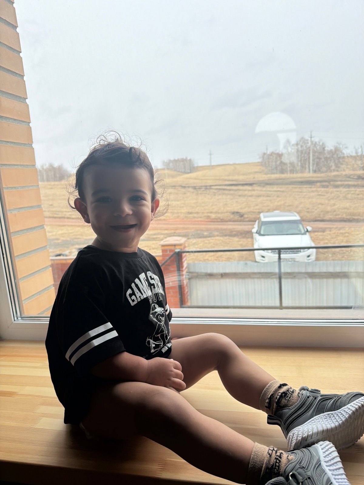 Child sits on windowsill in Krasnoyarsk wearing gaming shirt