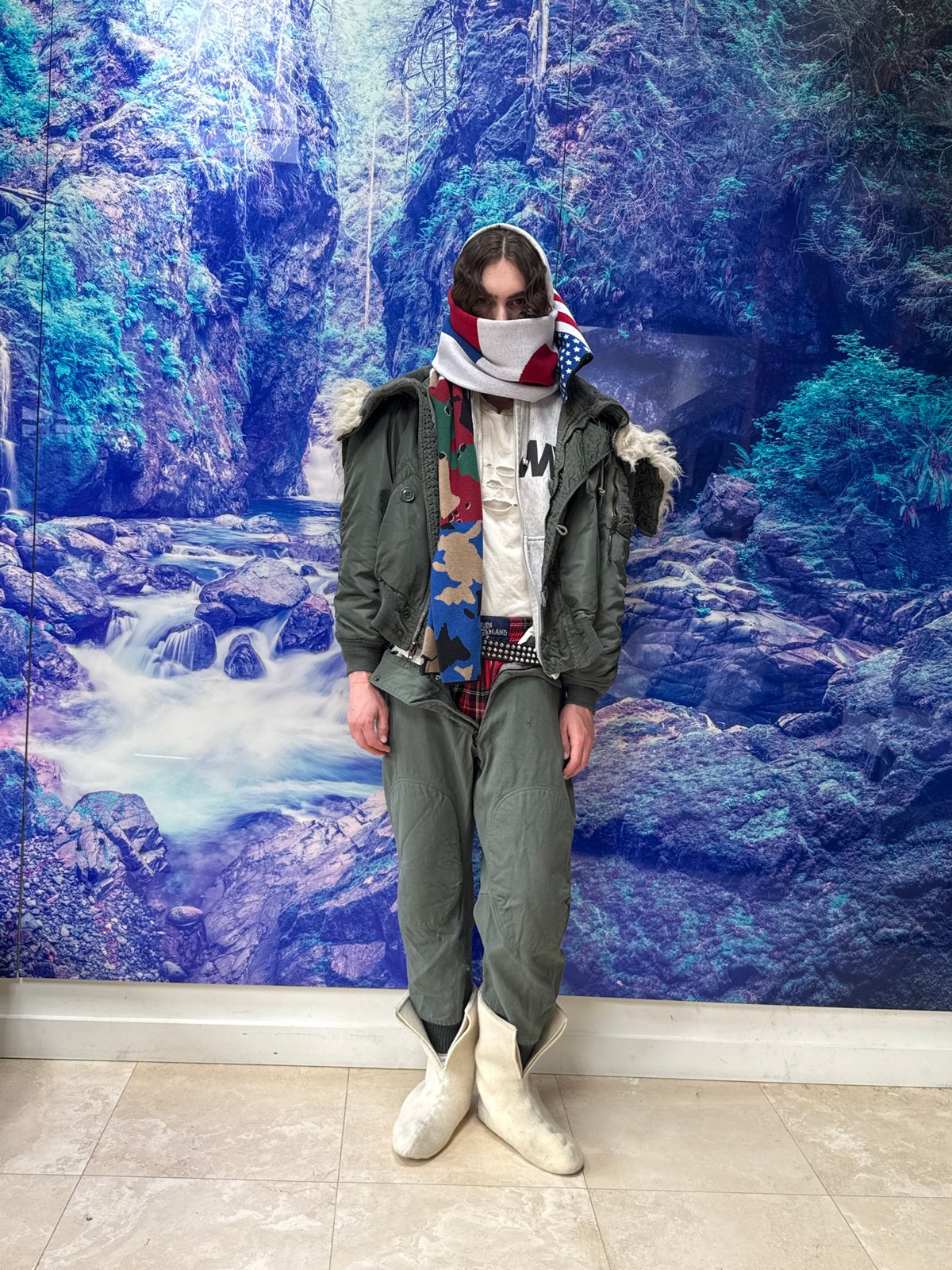 Person photographed in layered clothing against mountain artwork backdrop