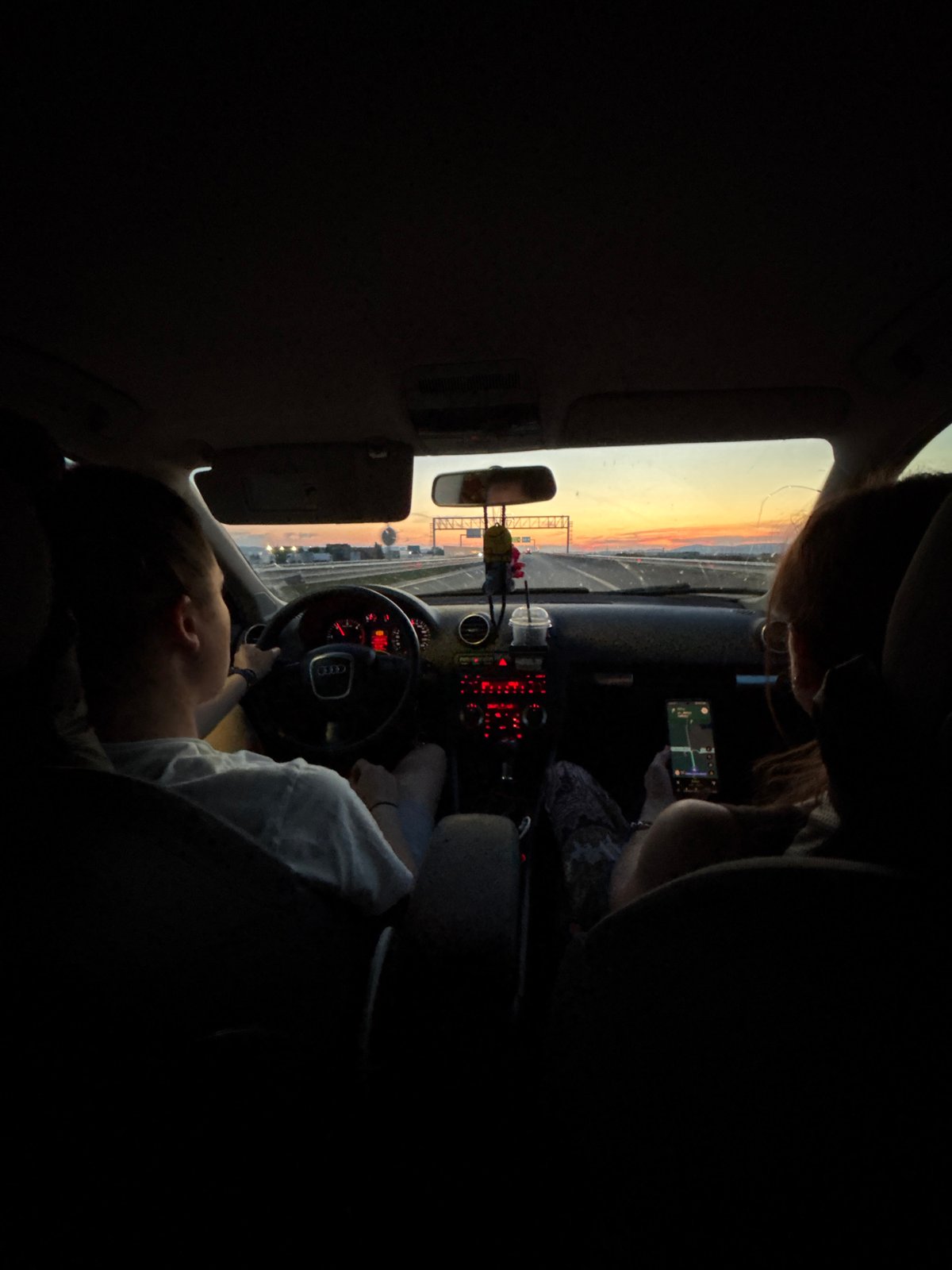 Two people drive through Sofia at sunset, passenger uses phone