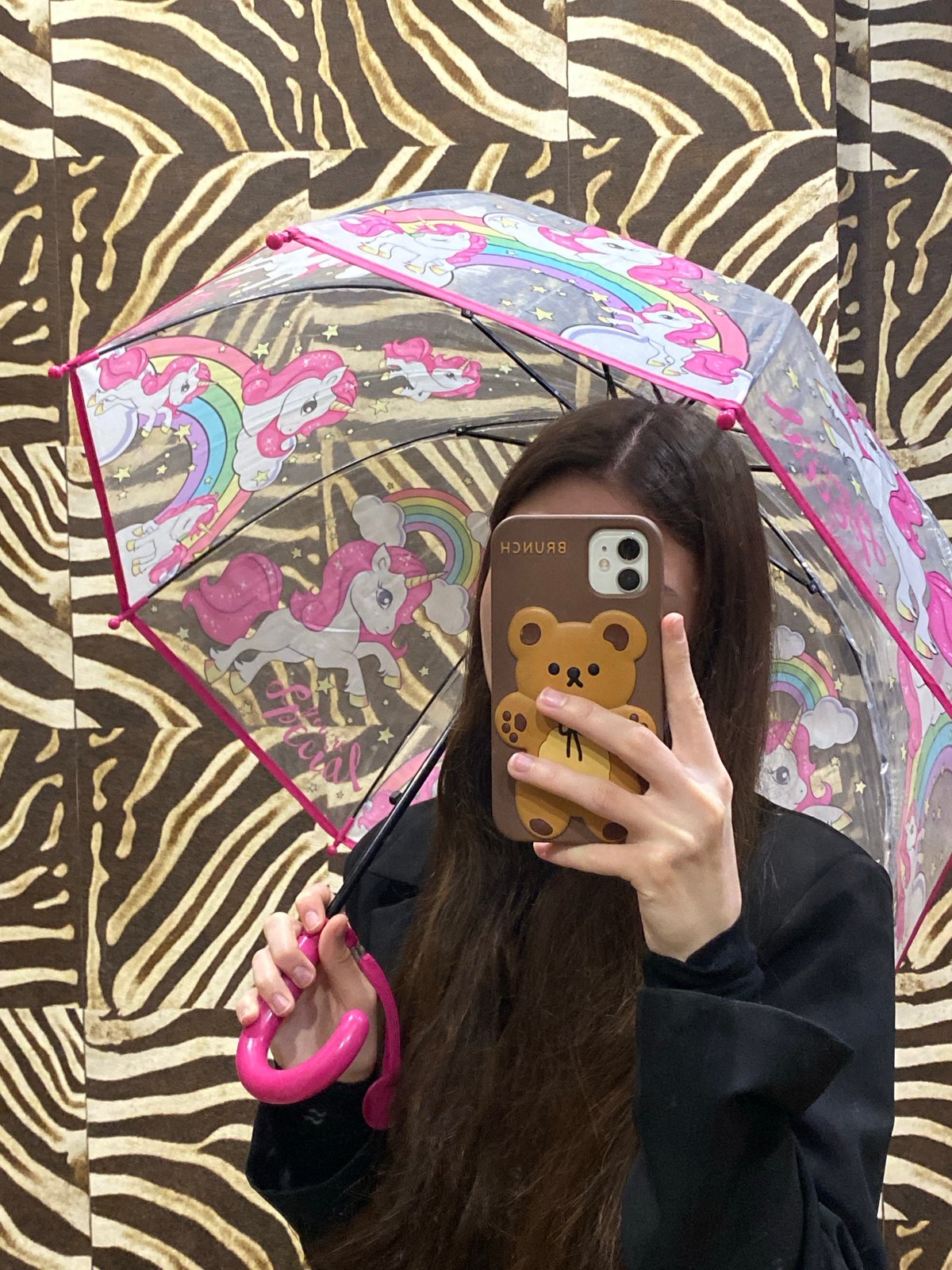 Person takes selfie with unicorn umbrella against zebra backdrop