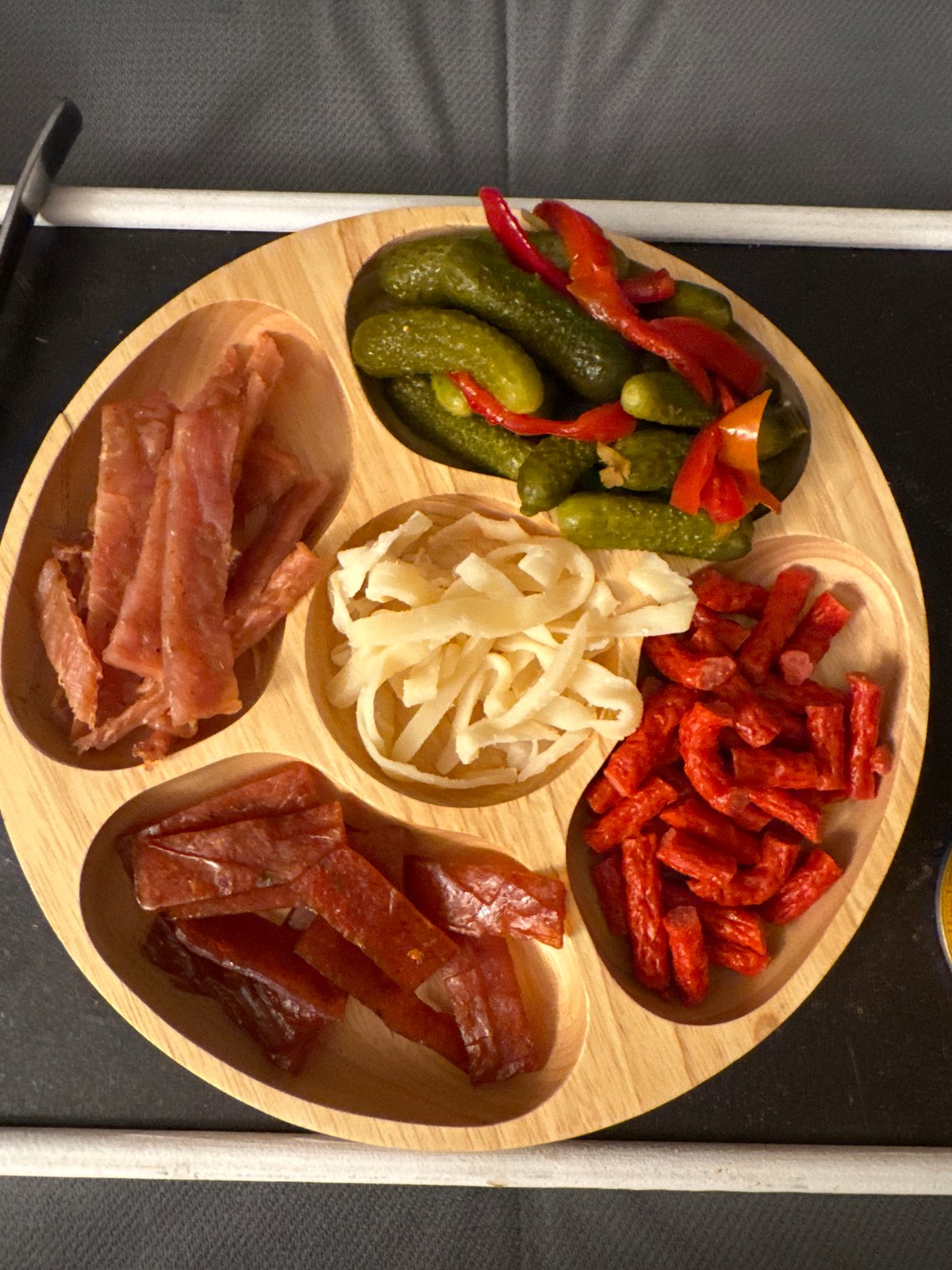 Sectioned wooden food tray with pickles and sausages documented