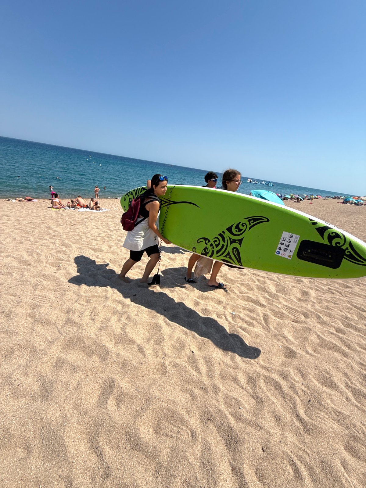 Green surfboard heads across a sunny Blanes beach