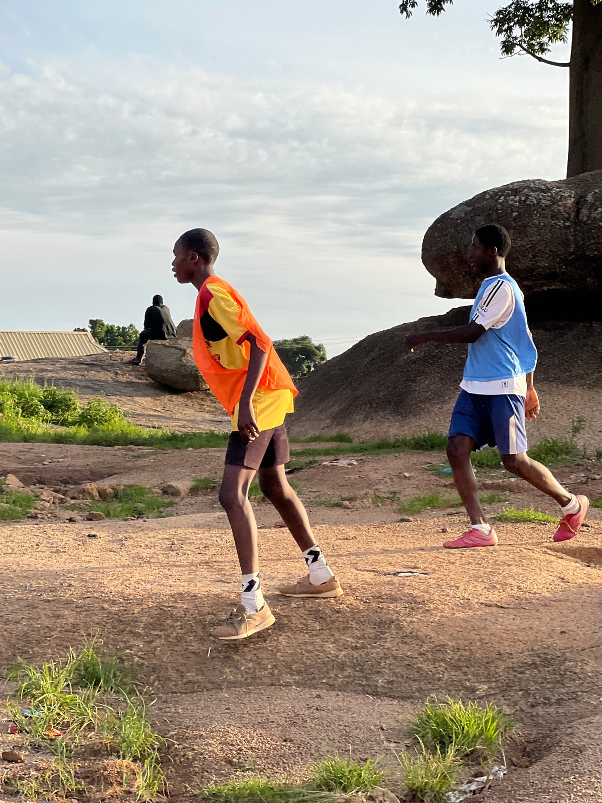 Pickup football on a dusty Jos field at golden hour