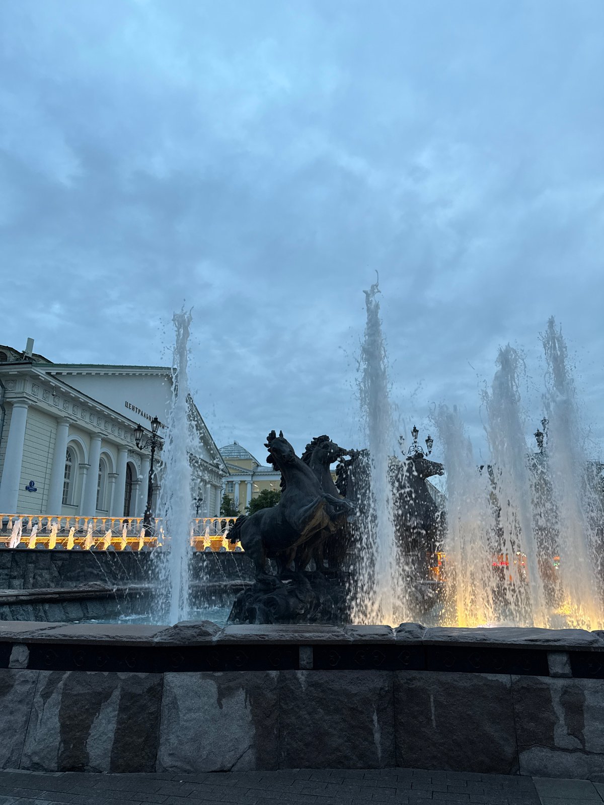 Tourists photograph Moscow's Manege Square fountain during evening visit