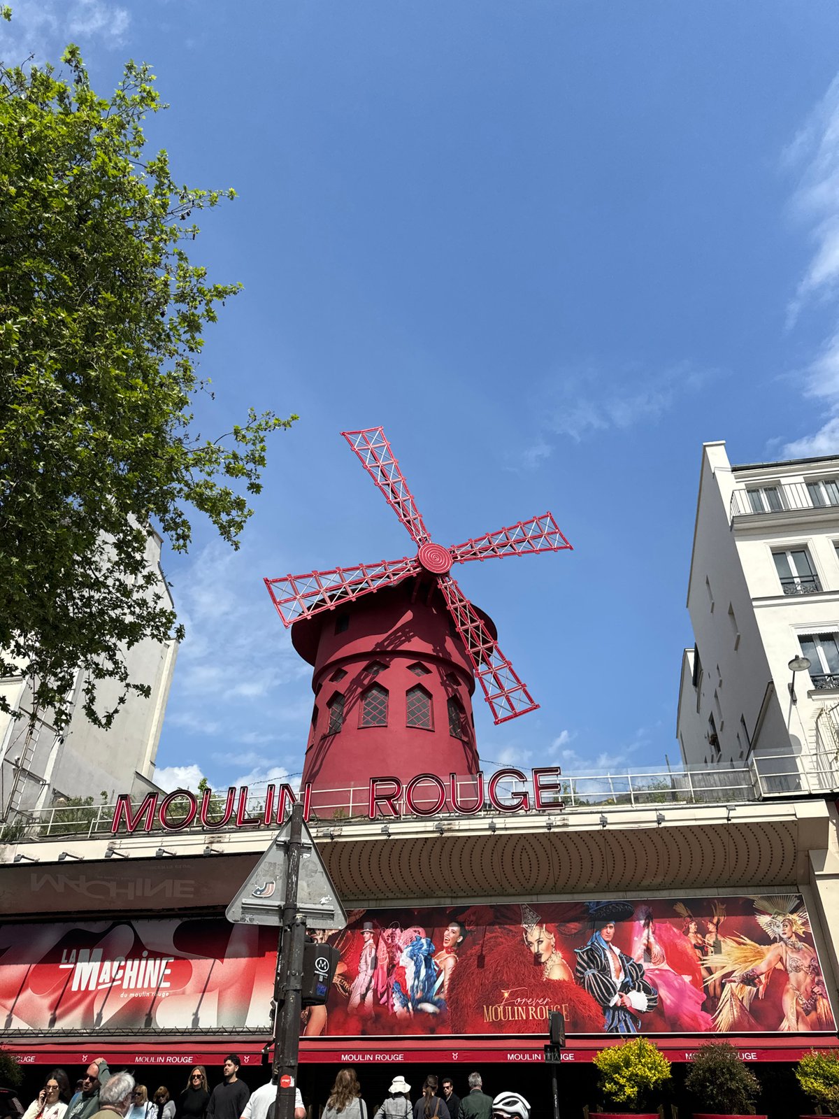 Tourist photographs iconic Moulin Rouge on sunny Paris afternoon