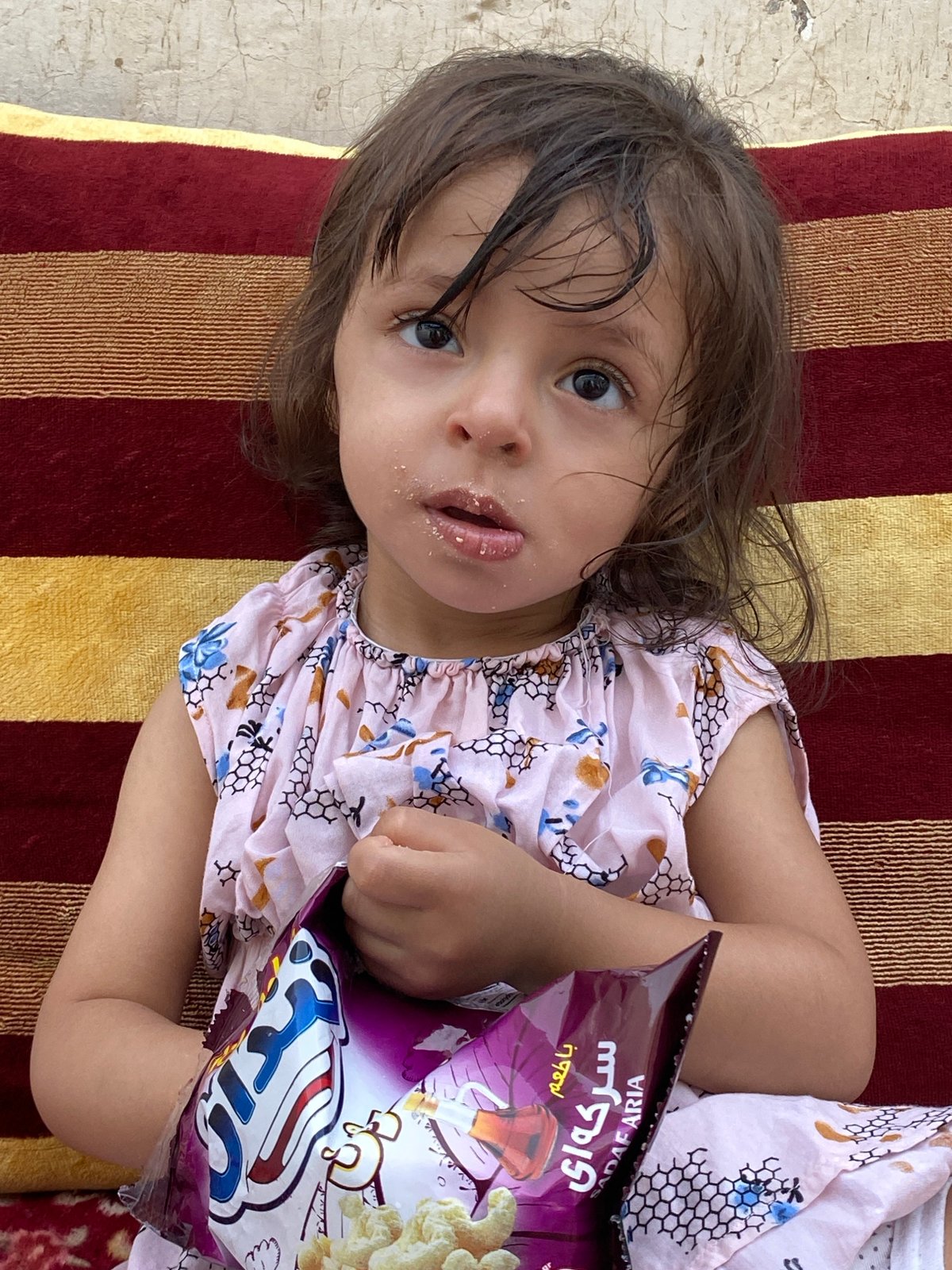 Child snacking on a striped cushion in Kandahar