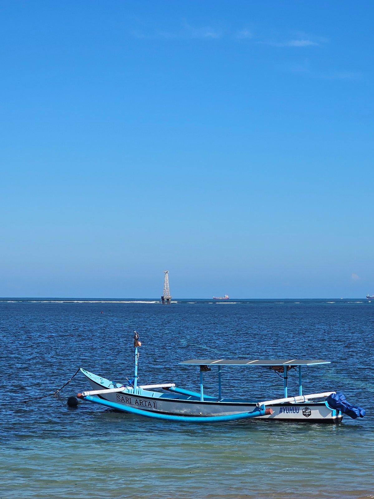 Quiet morning at Sanur Beach, boats, shade trees, and calm water.