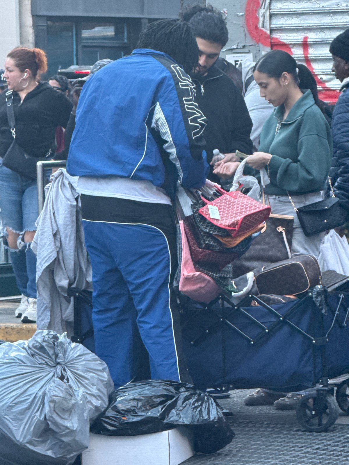 People queue on NYC sidewalk with belongings near shuttered storefront