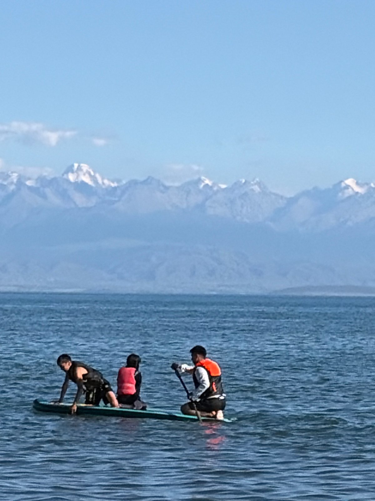 Mountain lake beach day: paddleboards, horses, and snow-capped peaks