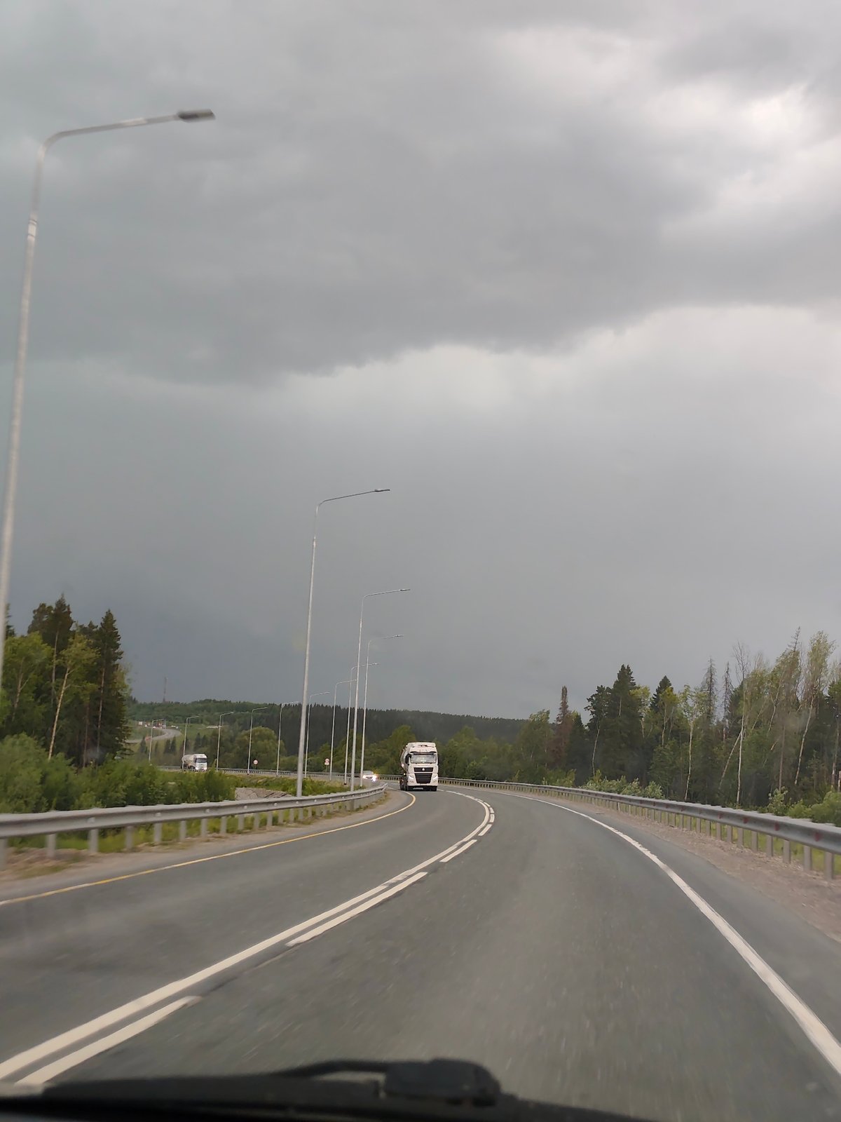 White truck travels forest road in Chusovskoye under cloudy skies