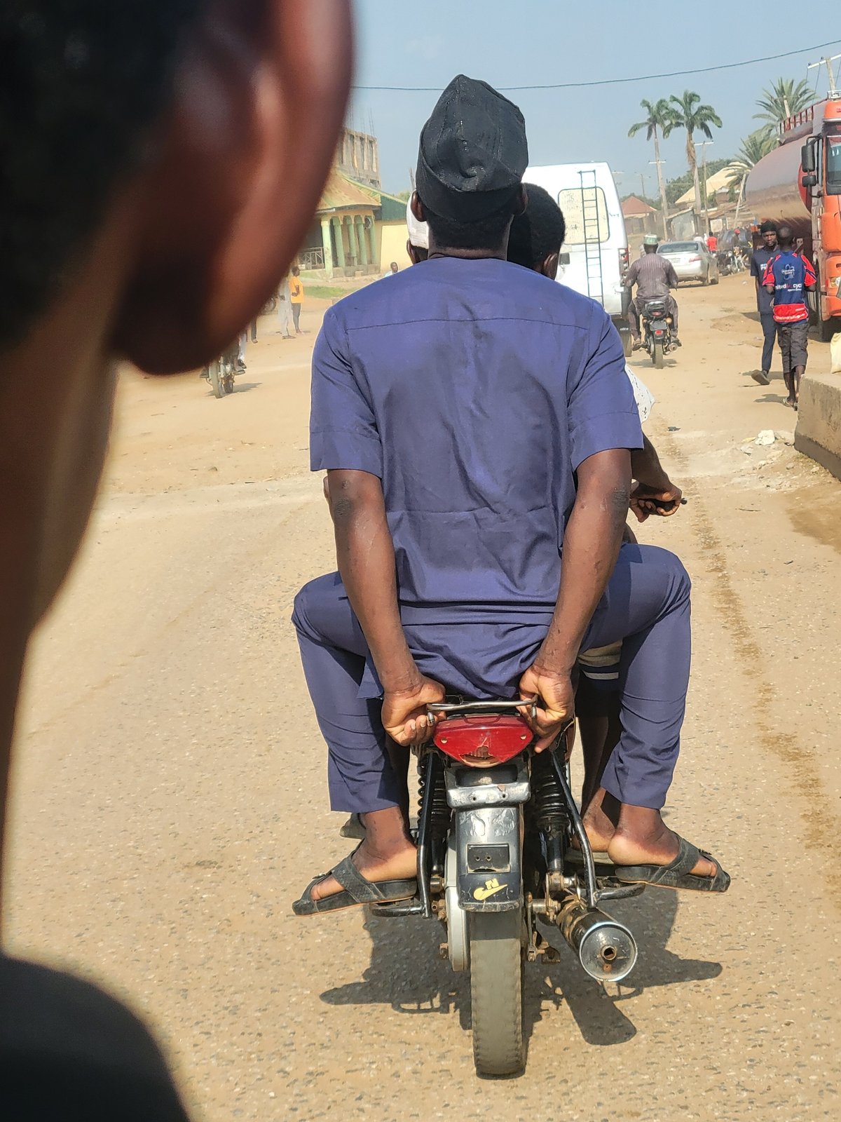 Motorcycle riders travel dirt road near Keffi college