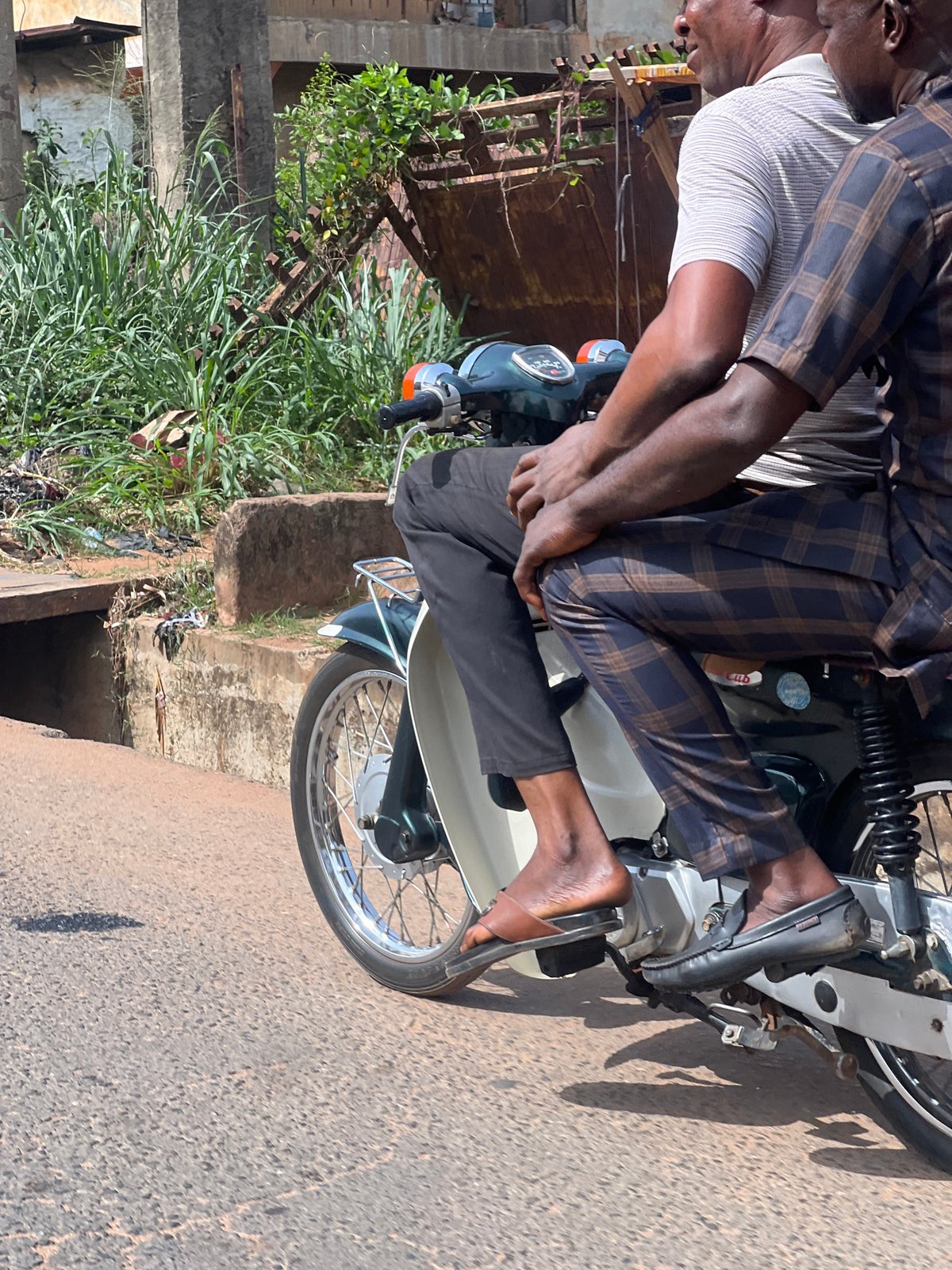Two men ride motorcycle on road in Nkpor, Nigeria