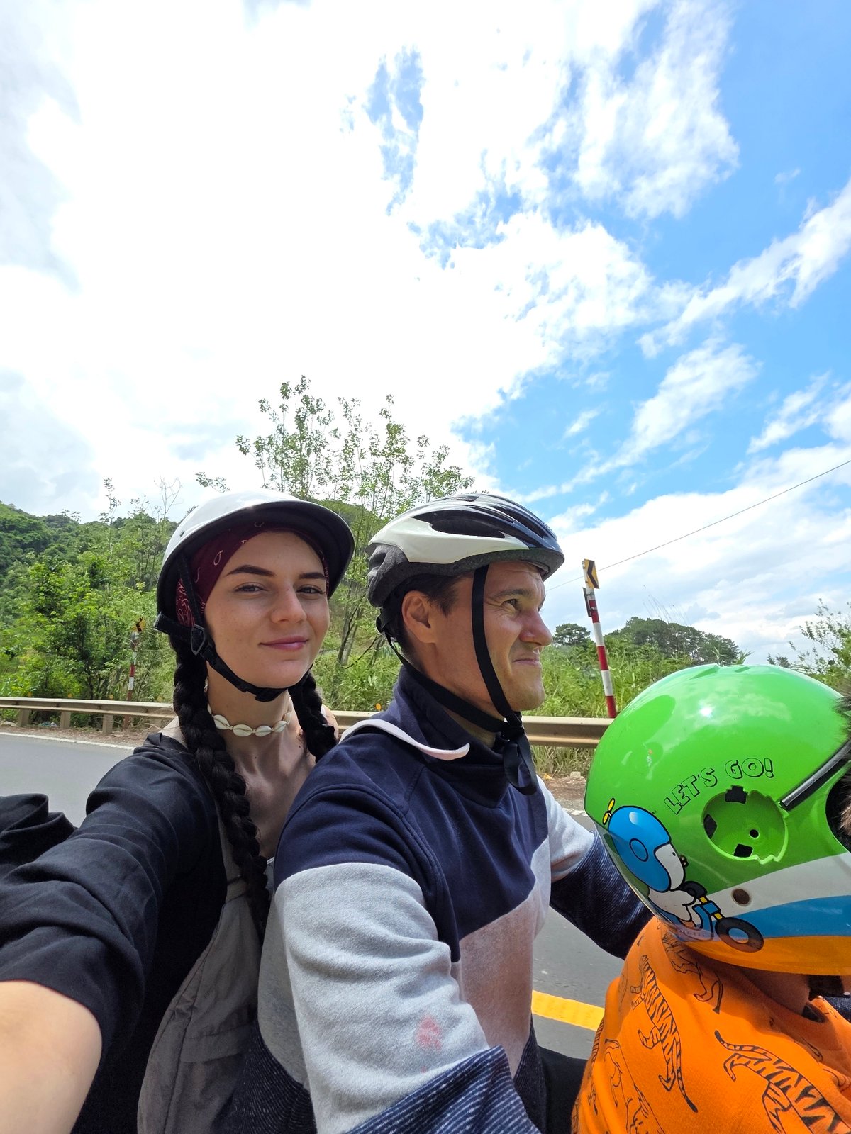 Three helmet-wearing riders travel mountain road in rural Vietnam