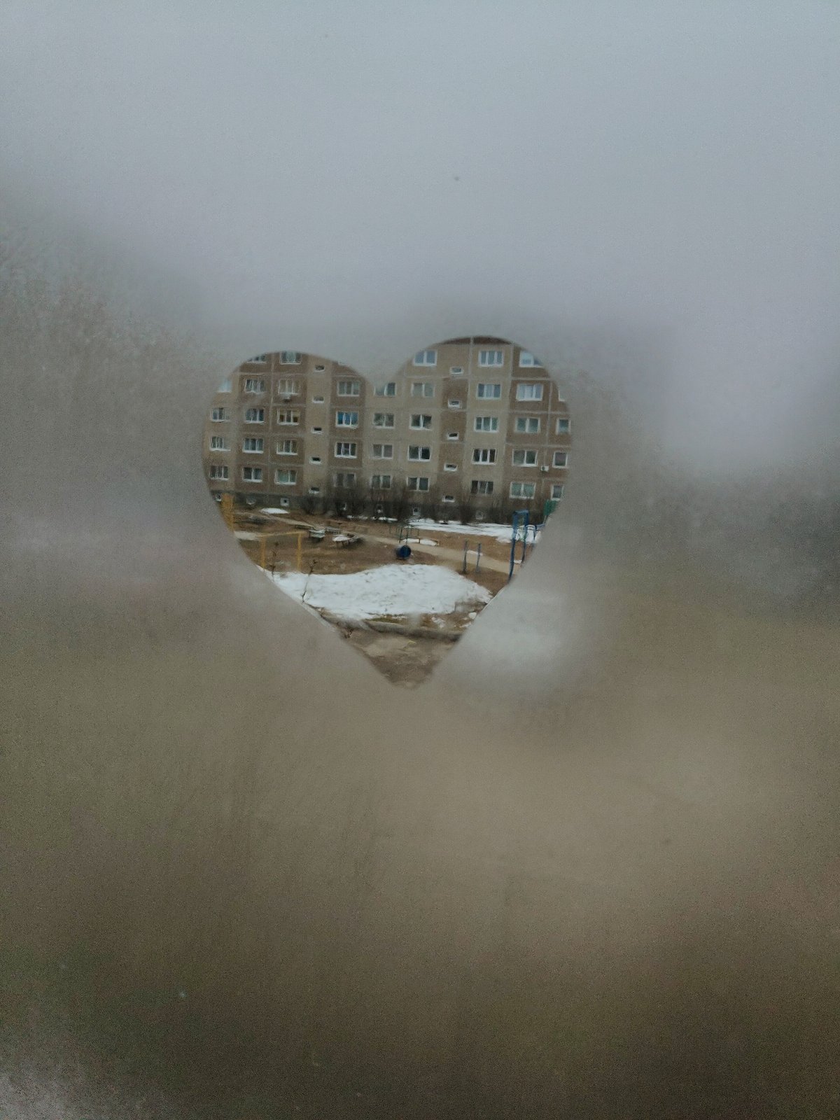 Heart traced in window condensation frames apartment building view