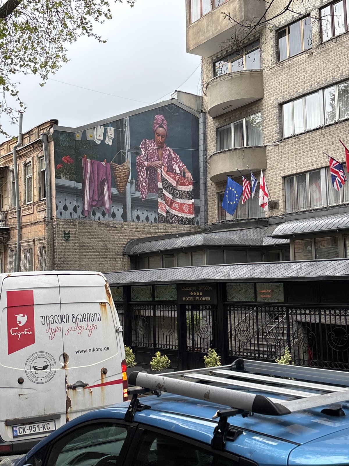 Traditional woman mural spotted on Tbilisi street with flags