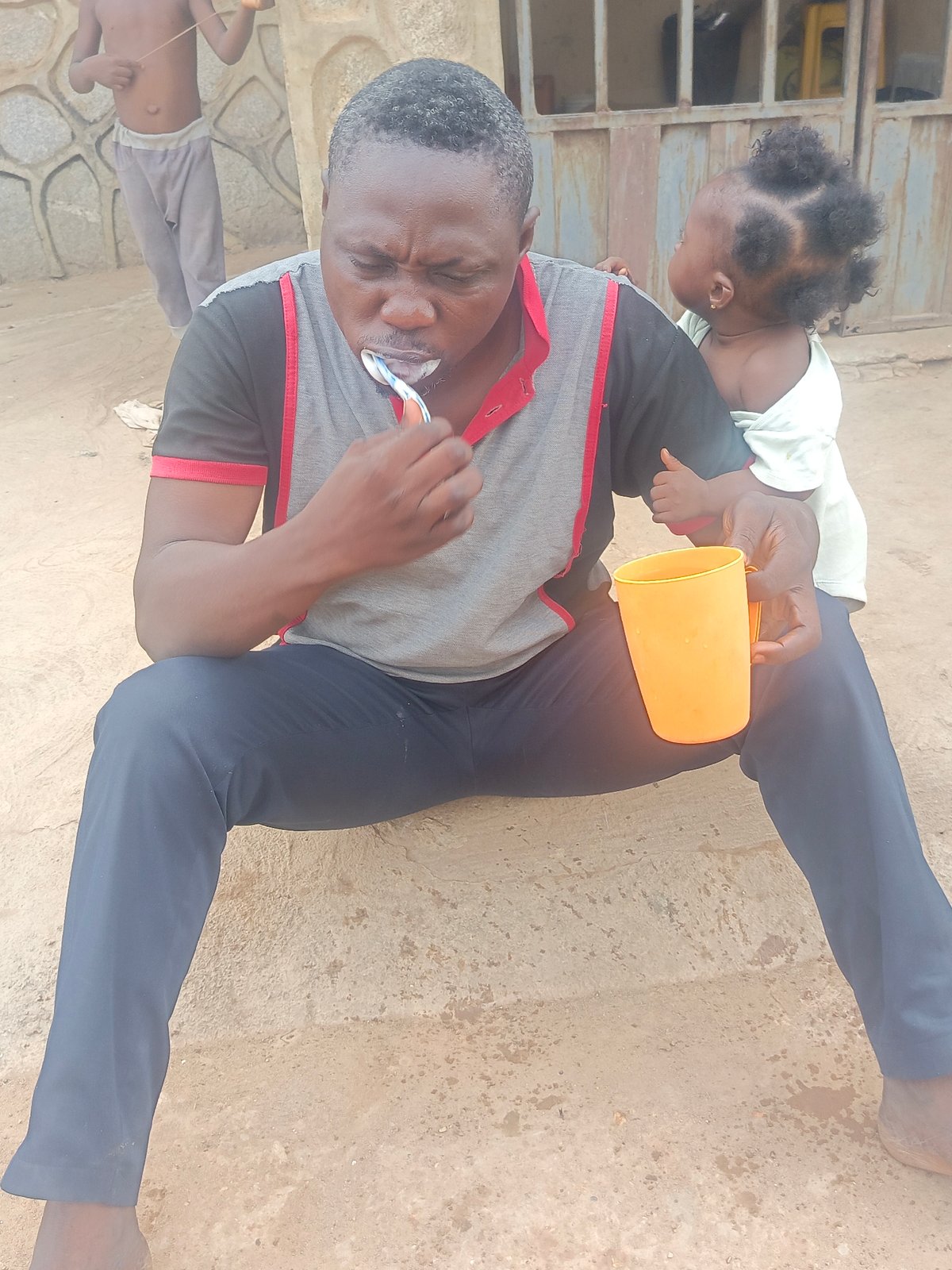 Man brushes teeth outdoors in Akwanga, child watches