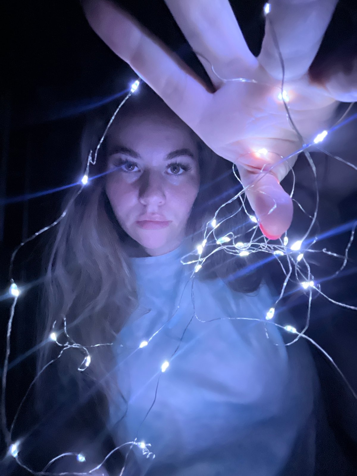 Woman poses with fairy lights in darkened space