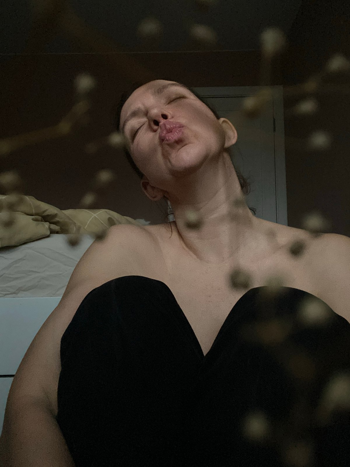 Woman poses on bed in dimly lit bedroom, Chaikovsky