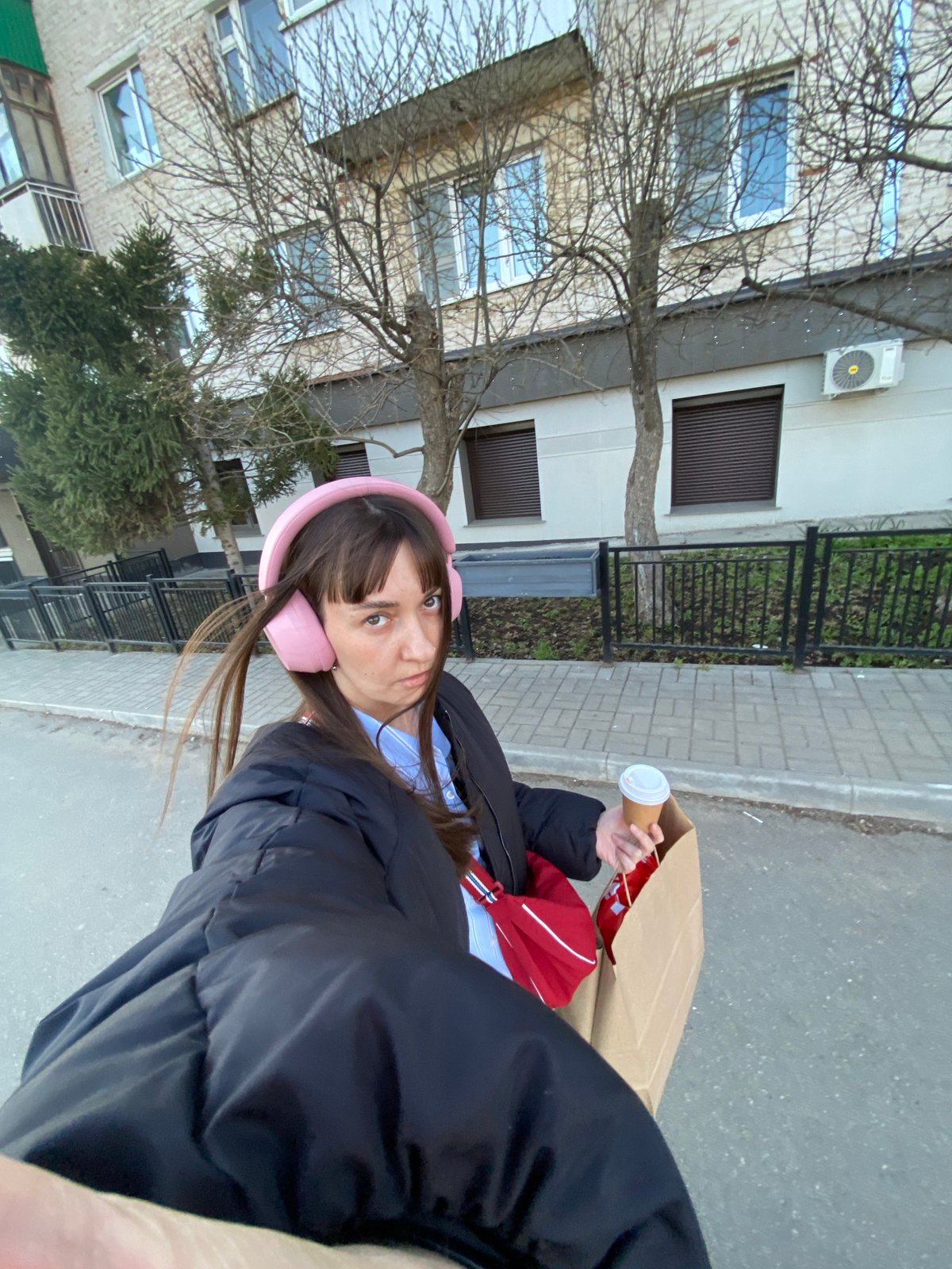 Woman with pink headphones holds coffee outside Votkinsk building