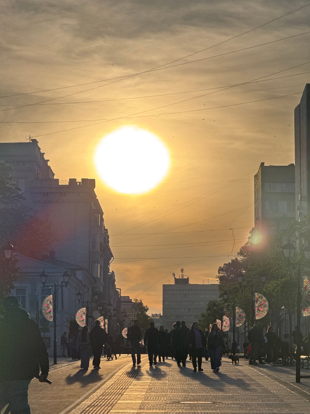 Pedestrians walk Saratov street during golden hour sunset
