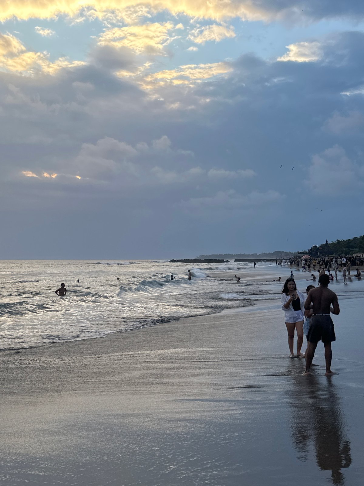 Surfers and beachgoers fill a North Kuta shore on an overcast morning