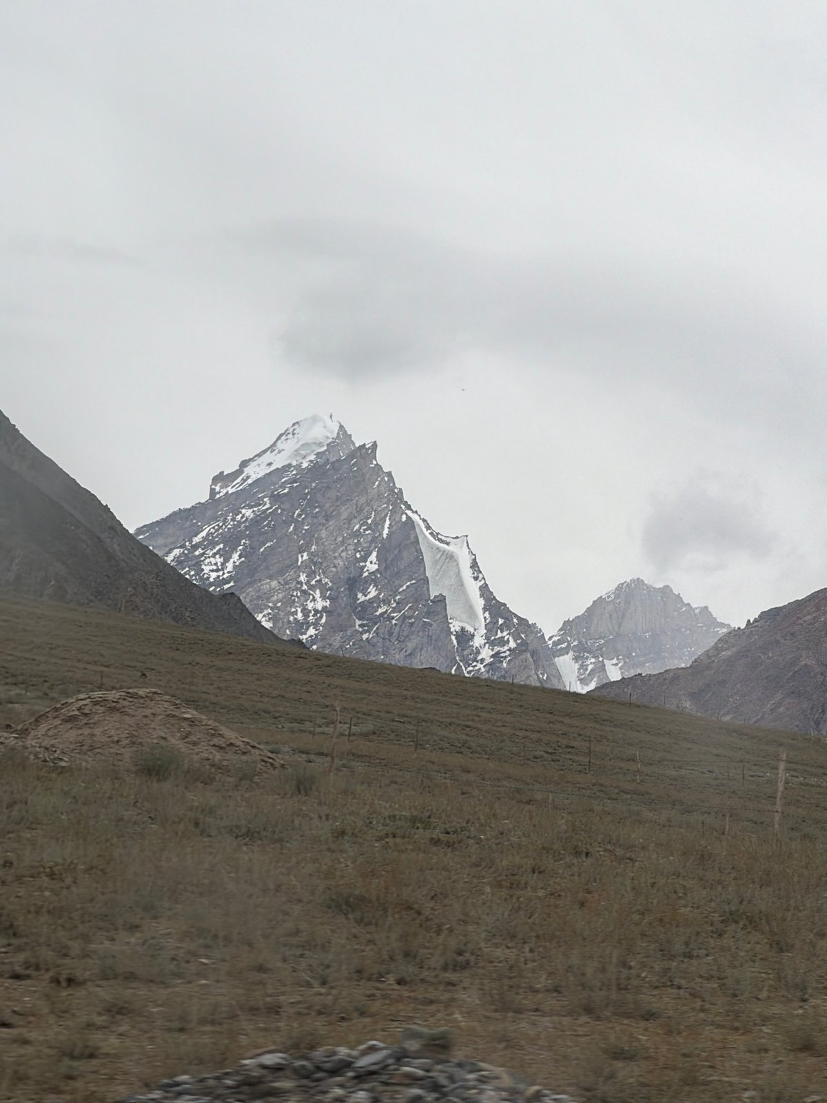 Barren mountain slope with wire fence under cloudy skies, Pibiting