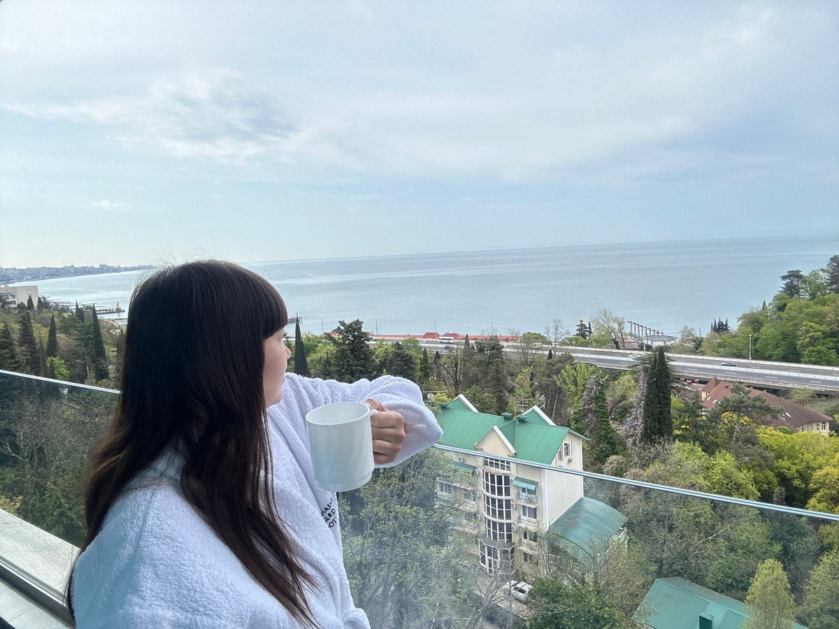 Woman enjoys morning coffee overlooking Sochi waterfront from balcony