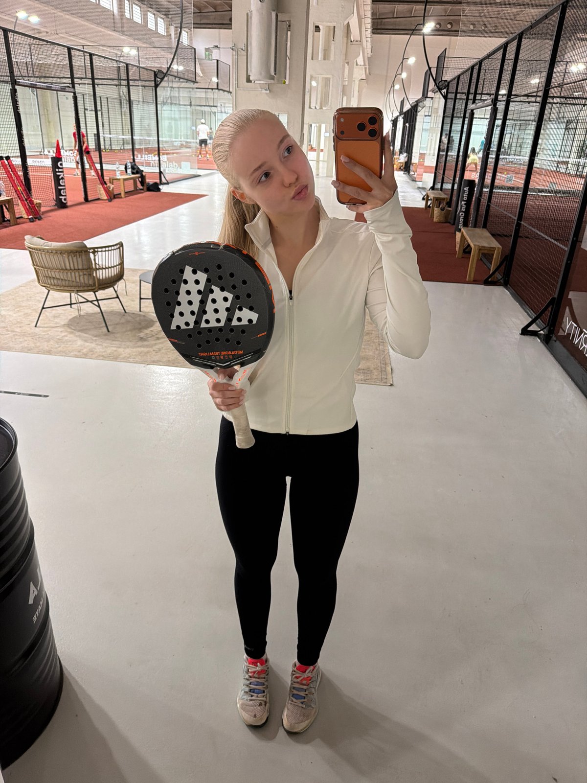 Woman takes selfies during padel tennis session at indoor facility
