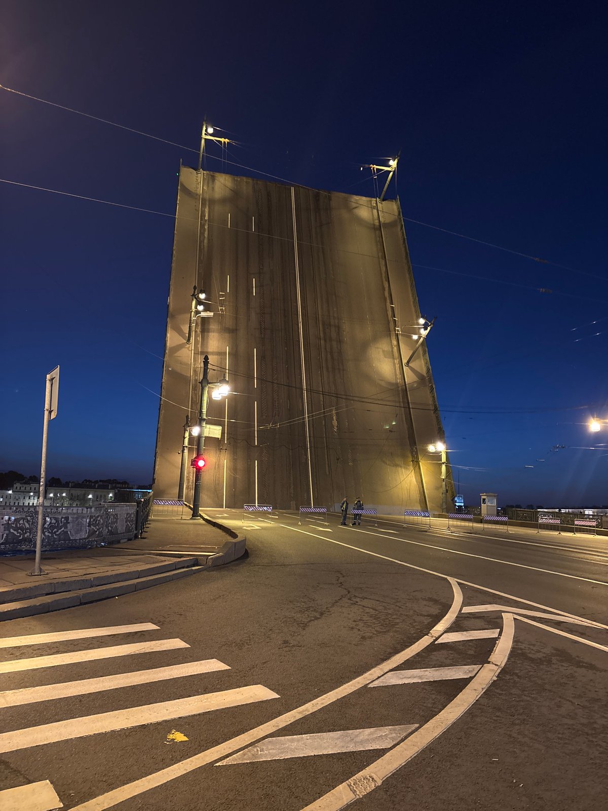Drawbridge raised at night, illuminated by streetlights over water
