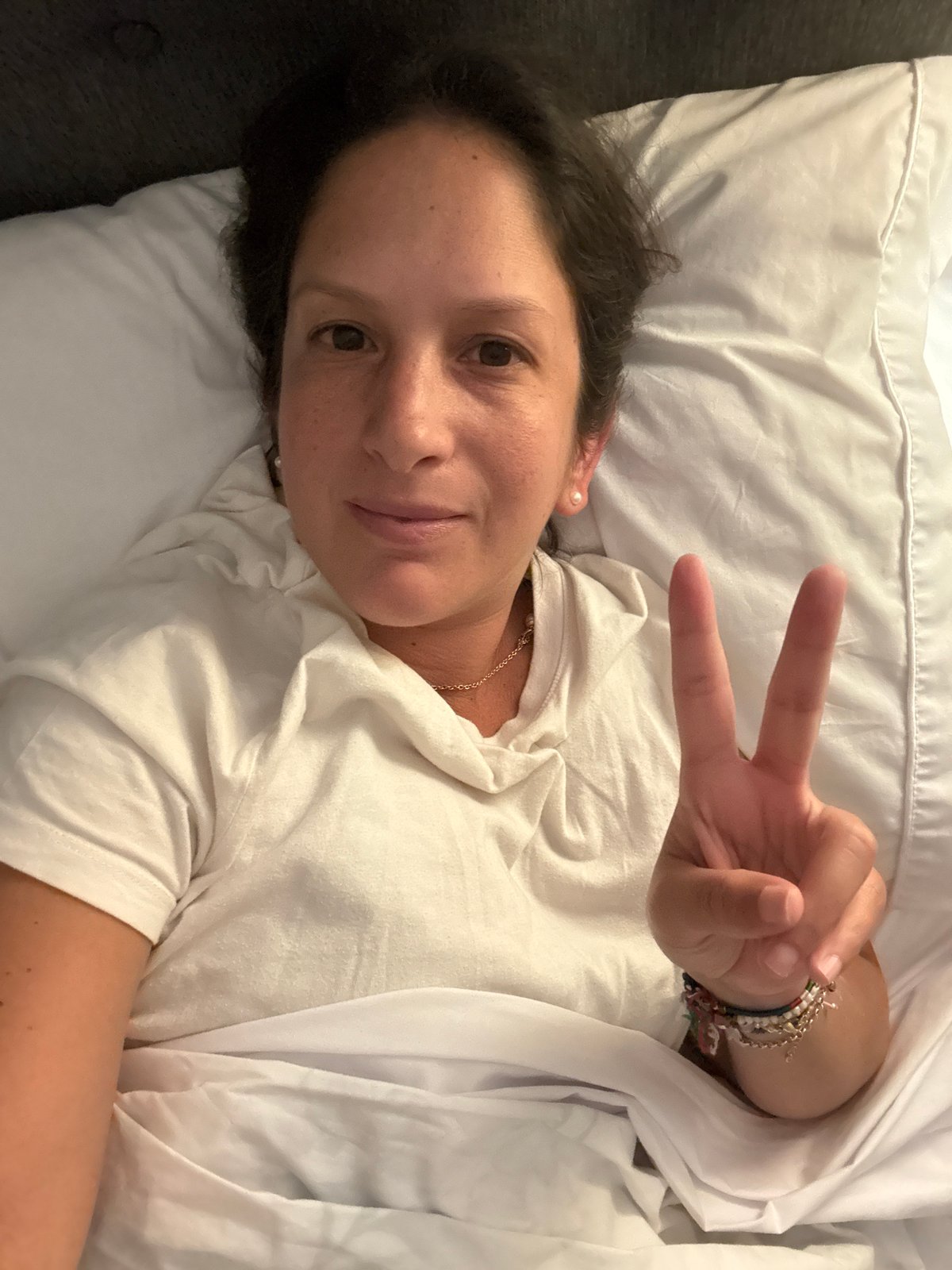 Woman makes peace sign gesture in bed in San Isidro