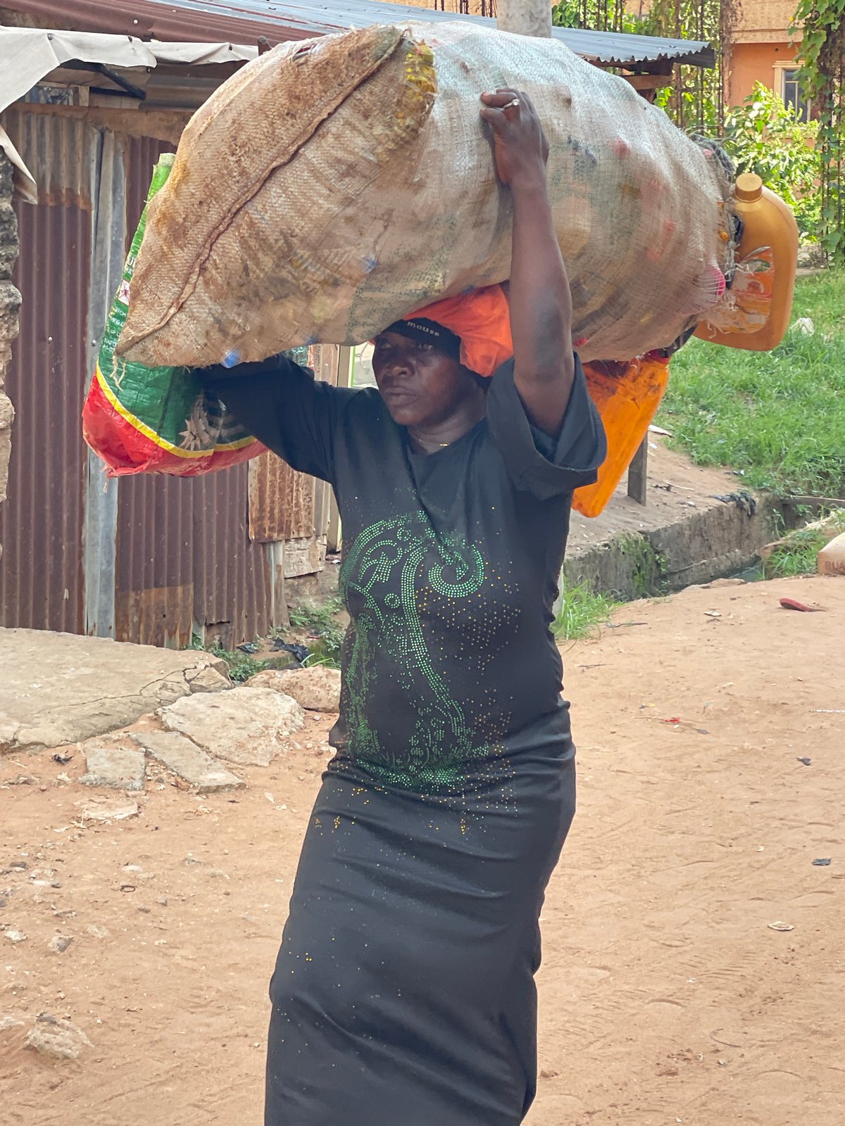 Woman carries recyclables in burlap sack in Nkpor, Nigeria